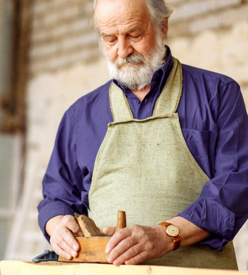 senior gentleman wearing an apron crafts a small sculpture